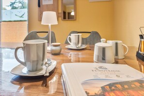 Een hotelkamer met een eettafel, voorzien van witte mokken, een lepel en een menukaart.