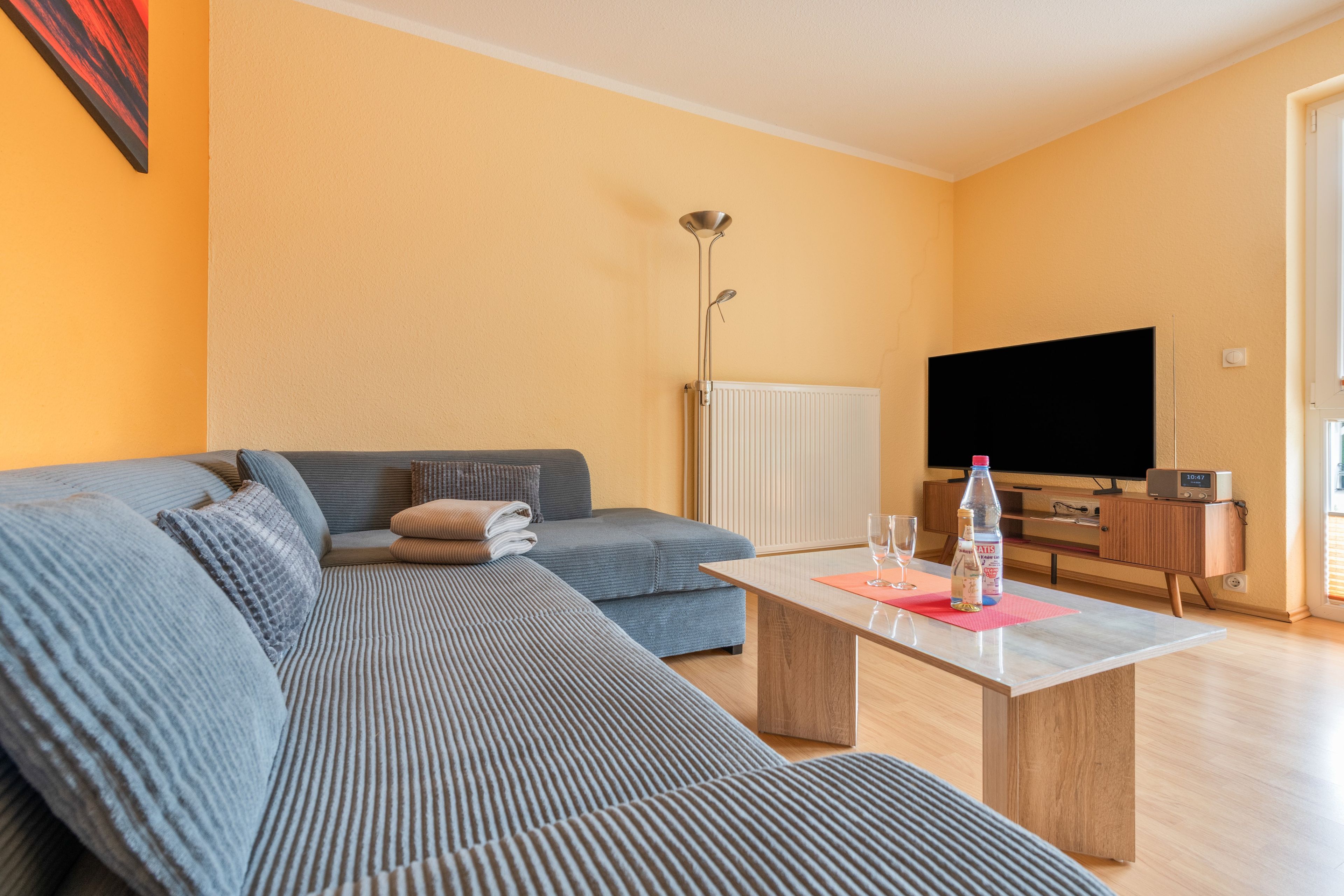 Ein modernes Wohnzimmer mit einem Ecksofa, einem Flachbildfernseher, einem Couchtisch und einer Heizung.