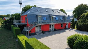 A two-story building with a red facade, a grey roof, and a staircase leading to the upper floor.