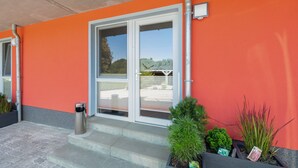 Ein Gebäudeeingang mit roter Fassade, einer Glastür und Stufen, die hinaufführen.