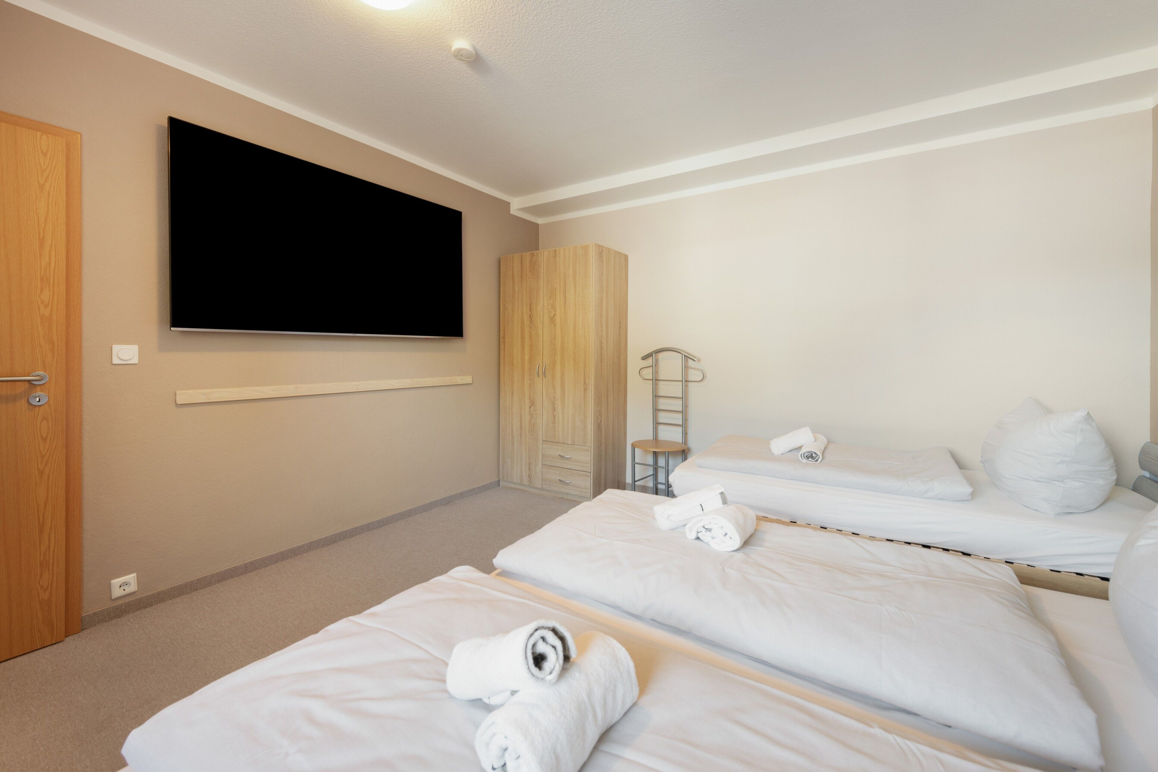 Quarto de hotel com duas camas, televisão, guarda-roupa e uma mesinha.