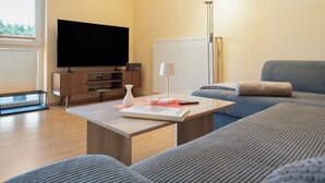 Ein modernes Wohnzimmer mit einem Flachbildfernseher, einem Couchtisch mit einem Buch und einer Vase, einer Couch und einer Lampe.