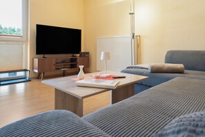 A modern living room with a flat-screen TV, a coffee table with a book and a vase, a sofa, and a lamp. - Apartment 'Fewotraum Müritz Möwe 2' with Private Terrace and Wi-Fi (Röbel)