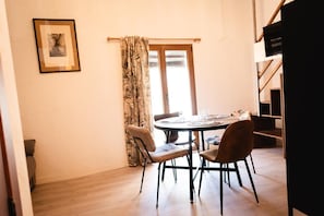 Un comedor con una mesa redonda, cuatro sillas, una ventana con cortinas y un cuadro en la pared.