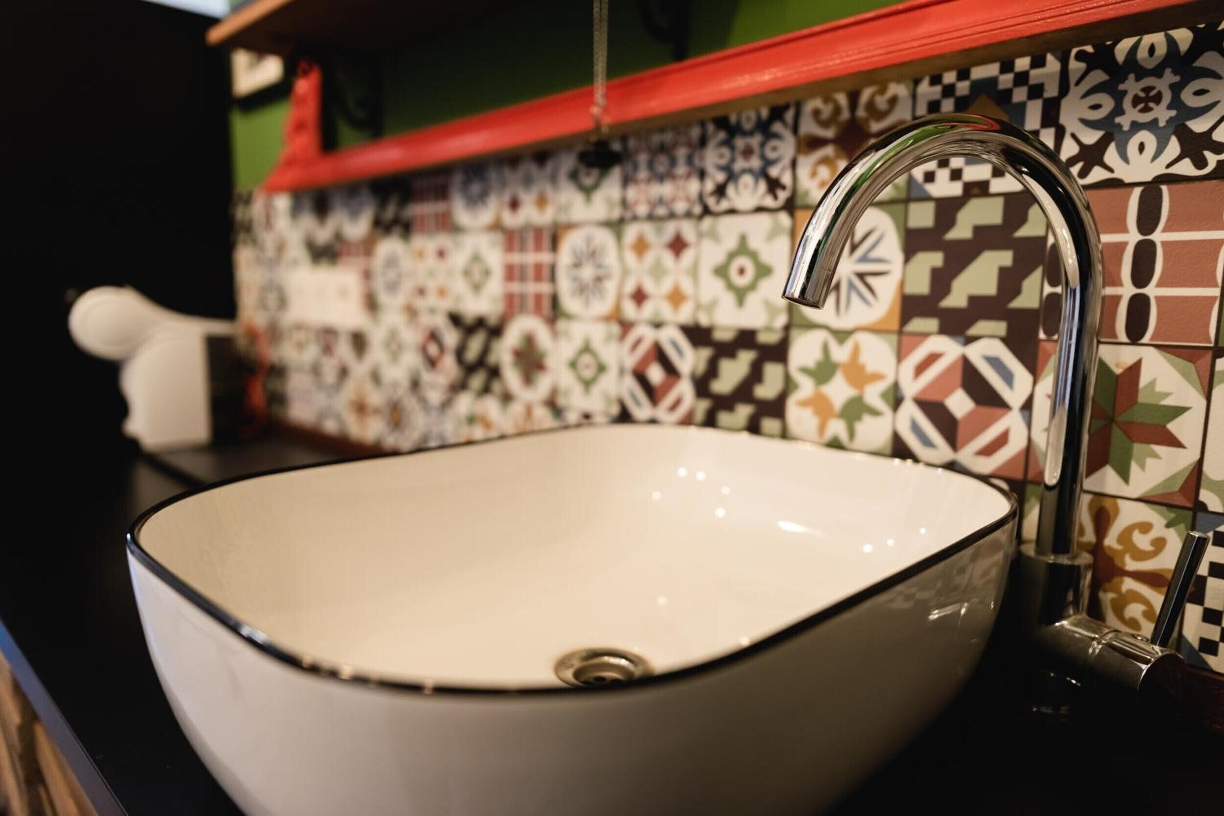 Un lavamanos de cerámica blanca con un solo grifo, frente a un salpicadero de azulejos con diversos diseños.