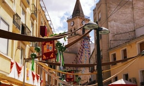 Una calle estrecha con edificios, una torre con relojes y adornos colgantes.