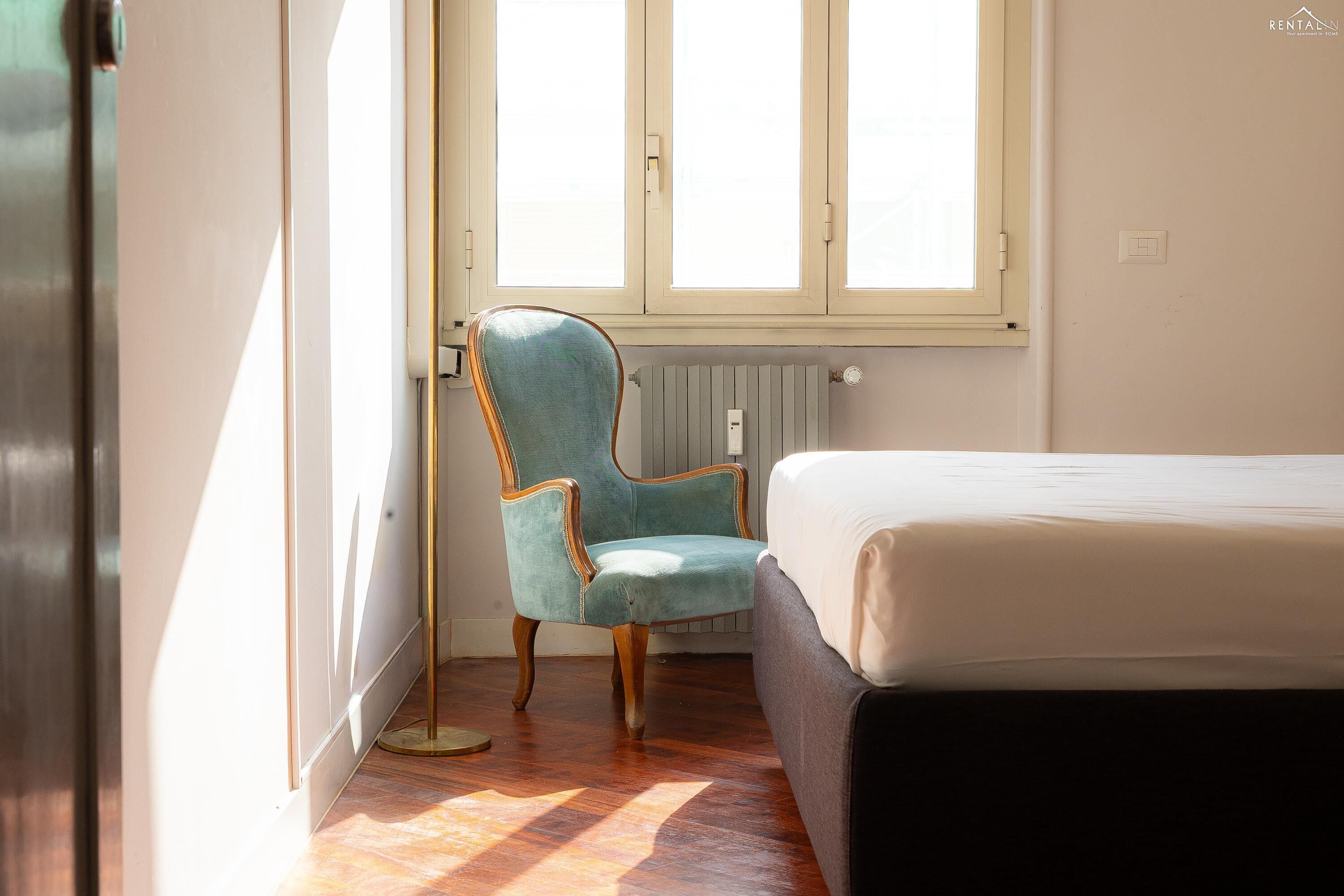 A bedroom with a bed, a chair, a radiator, and a window.