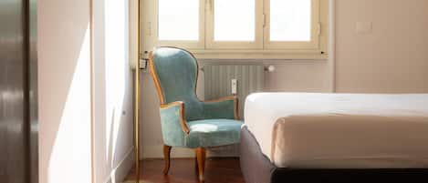 A bedroom with a bed, a chair, a radiator, and a window.
