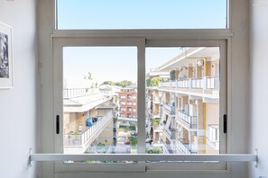 A view through a sliding glass door of a multi-story residential building with balconies, outdoor seating, and a clear sky. - Francesco Terrace apartment (Rome)