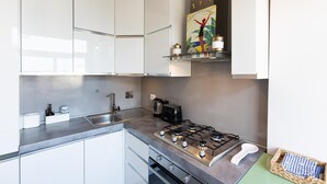 Une cuisine moderne avec des meubles blancs, une cuisinière à gaz, une machine à café et un panneau décoratif au-dessus de la cuisinière.