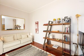 A living room with a white sofa, a wooden bookshelf, a mirror, and a floor lamp. - Francesco Terrace apartment (Rome)
