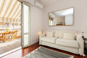 A room with a white sofa, a large mirror, and a view of an outdoor patio with wooden furniture. - Francesco Terrace apartment (Rome)