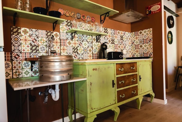 A kitchen with a tiled backsplash, a kettle, and a cabinet with drawers.