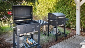 Ein Grill mit Seitenbrenner und Räucherofen, beide auf Rollständern, in einem Garten mit einem Pflasterweg.