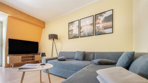 Ein modernes Wohnzimmer mit einem großen Flachbildfernseher, einer Couch, einer Stehlampe und drei gerahmten Bildern an der Wand.