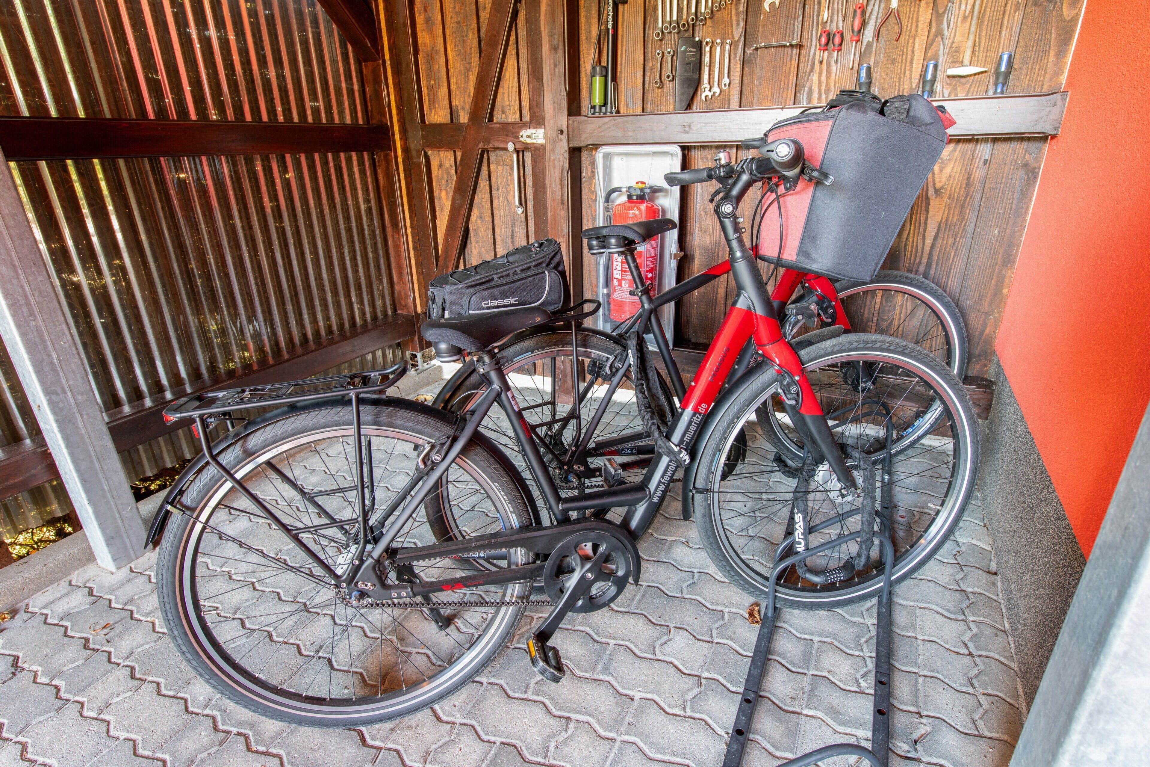 Una bicicleta estacionada en el interior, con una puerta de madera y un perchero para herramientas al fondo.