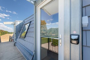Un bâtiment moderne doté d’une porte en verre, d’une rambarde en métal et offrant une vue sur un paysage composé d’arbres et de collines.