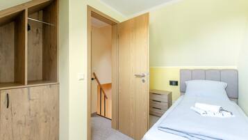 Quarto com cama, guarda-roupa de madeira, mesa de cabeceira e porta para outro cômodo.