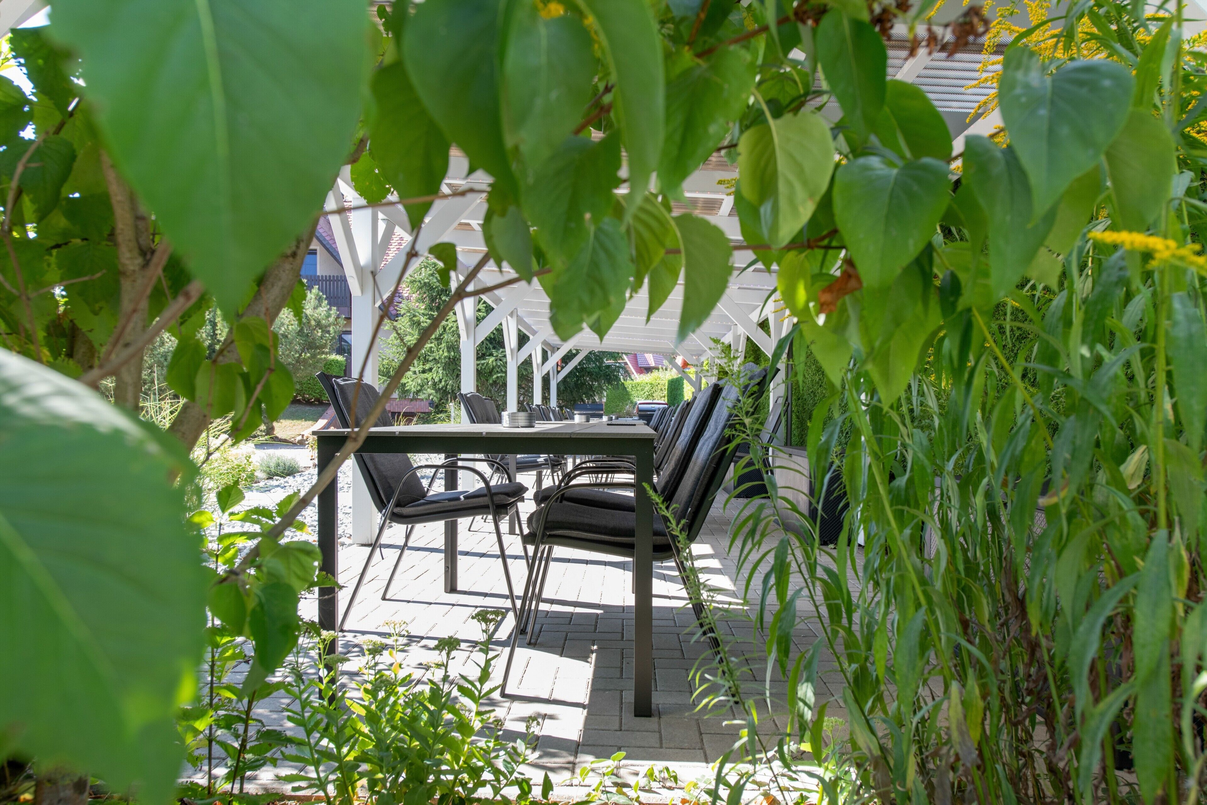 Eine sonnige Terrasse mit Tisch und Stühlen, umgeben von viel Grün.