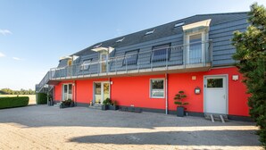 Ein zweistöckiges Gebäude mit roter Fassade, einem überdachten Balkon und einer Zuwegung mit Kies.