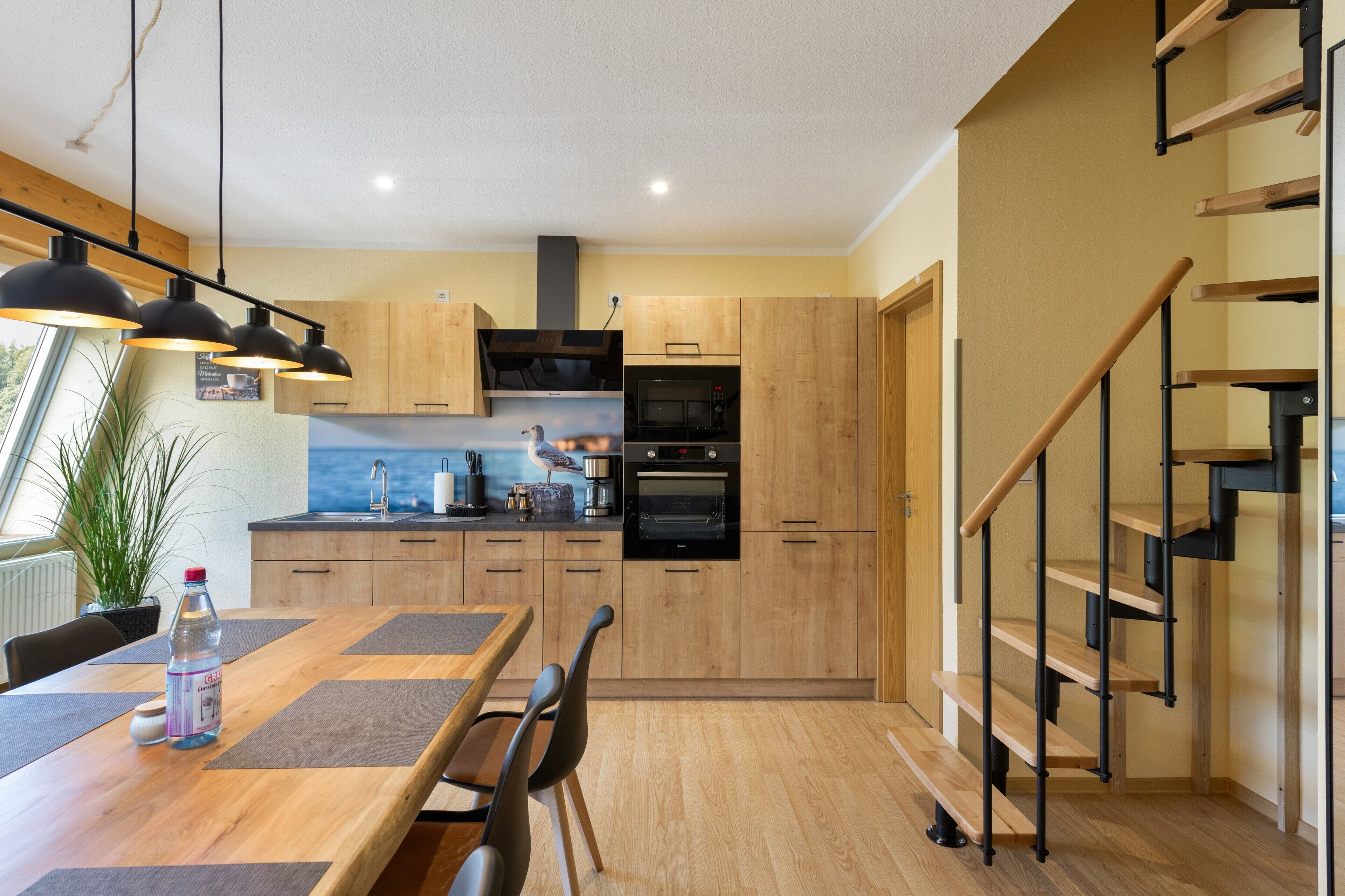 Eine moderne Küche mit Holzschränken, einem eingebauten Ofen und einem Essbereich mit einem Holztisch und Stühlen.