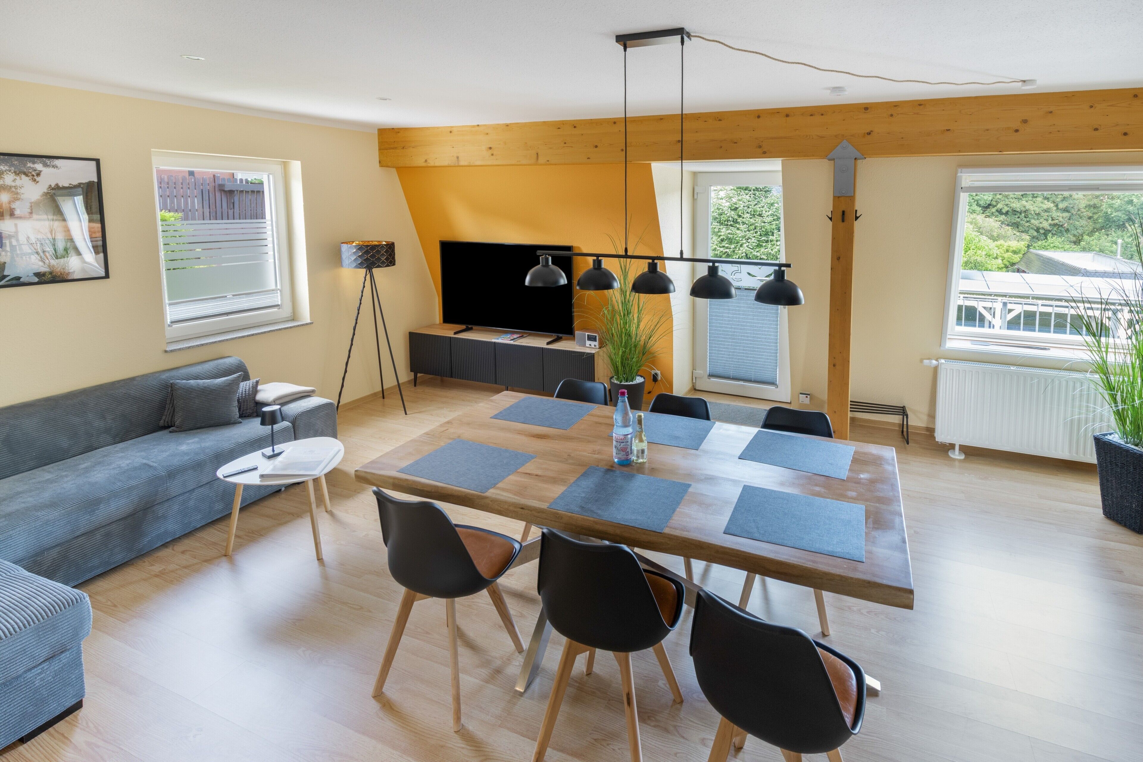Una sala de estar moderna con un sofá, una mesa de comedor con sillas, un televisor y una planta.