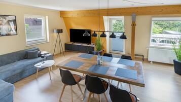 Una sala de estar moderna con un sofá, una mesa de comedor con sillas, un televisor y una planta.