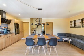 Eine moderne Küche mit Holzschränken, einem Einbauofen und einem Essbereich mit Holztisch und schwarzen Stühlen.