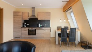 A modern kitchen with wooden cabinets, a built-in oven, and a dining area with a table and chairs. - Apartment 'Fewotraum Müritz Möwe 3' with Private Terrace and Wi-Fi (Röbel)
