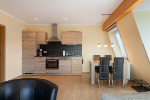 A modern kitchen with wooden cabinets, a built-in oven, and a dining area with a table and chairs. - Apartment 'Fewotraum Müritz Möwe 3' with Private Terrace and Wi-Fi (Röbel)