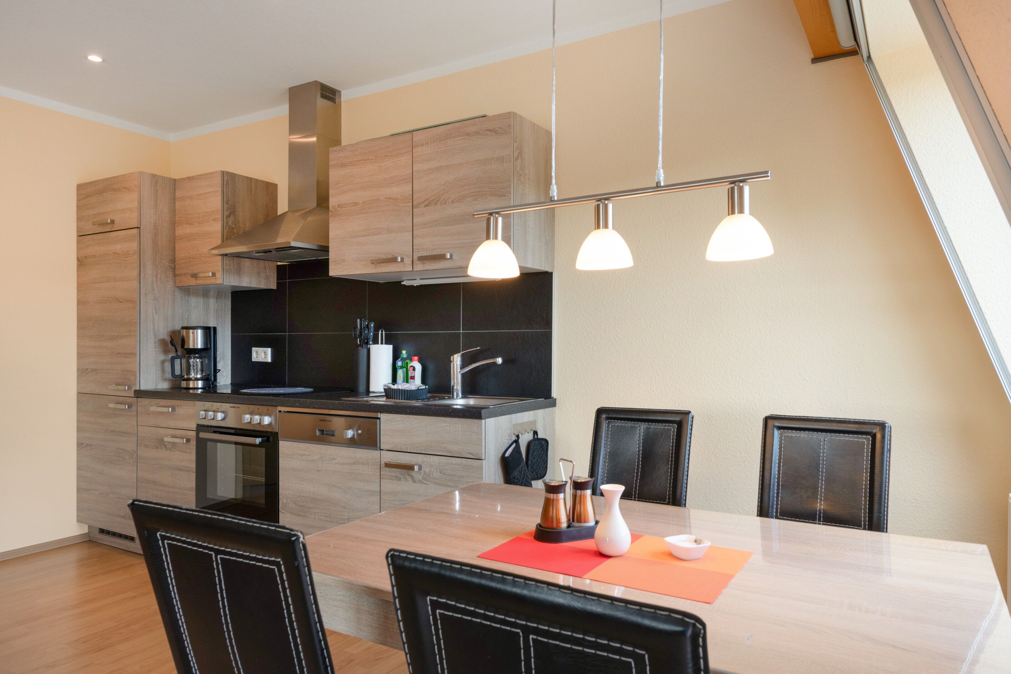 Eine moderne Küche mit Holzschränken, einem eingebauten Backofen und einem Essbereich mit Tisch und Stühlen.