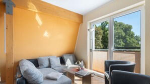 A modern living room with a sofa, a table, and chairs, a large window with a view of trees, and a wooden ceiling. - Apartment 'Fewotraum Müritz Möwe 3' with Private Terrace and Wi-Fi (Röbel)