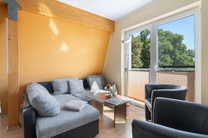 A modern living room with a sofa, a table, and chairs, a large window with a view of trees, and a wooden ceiling. - Apartment 'Fewotraum Müritz Möwe 3' with Private Terrace and Wi-Fi (Röbel)