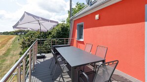 An outdoor patio with a table and chairs, a white umbrella, and a red building wall. - Apartment 'Fewotraum Müritz Möwe 3' with Private Terrace and Wi-Fi (Röbel)