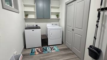 Une buanderie équipée d’un lave-linge, d’un sèche-linge et d’un balai appuyé contre le mur.