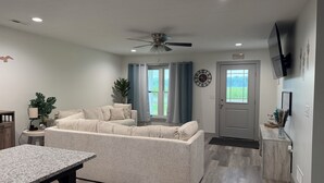 A modern living room with a sectional sofa, a dining table, a ceiling fan, and a view of the outdoors through a window. -  "Last Light", This Perfect 3-bedroom, 2 bath cottage in quaint GOTL. (Geneva)