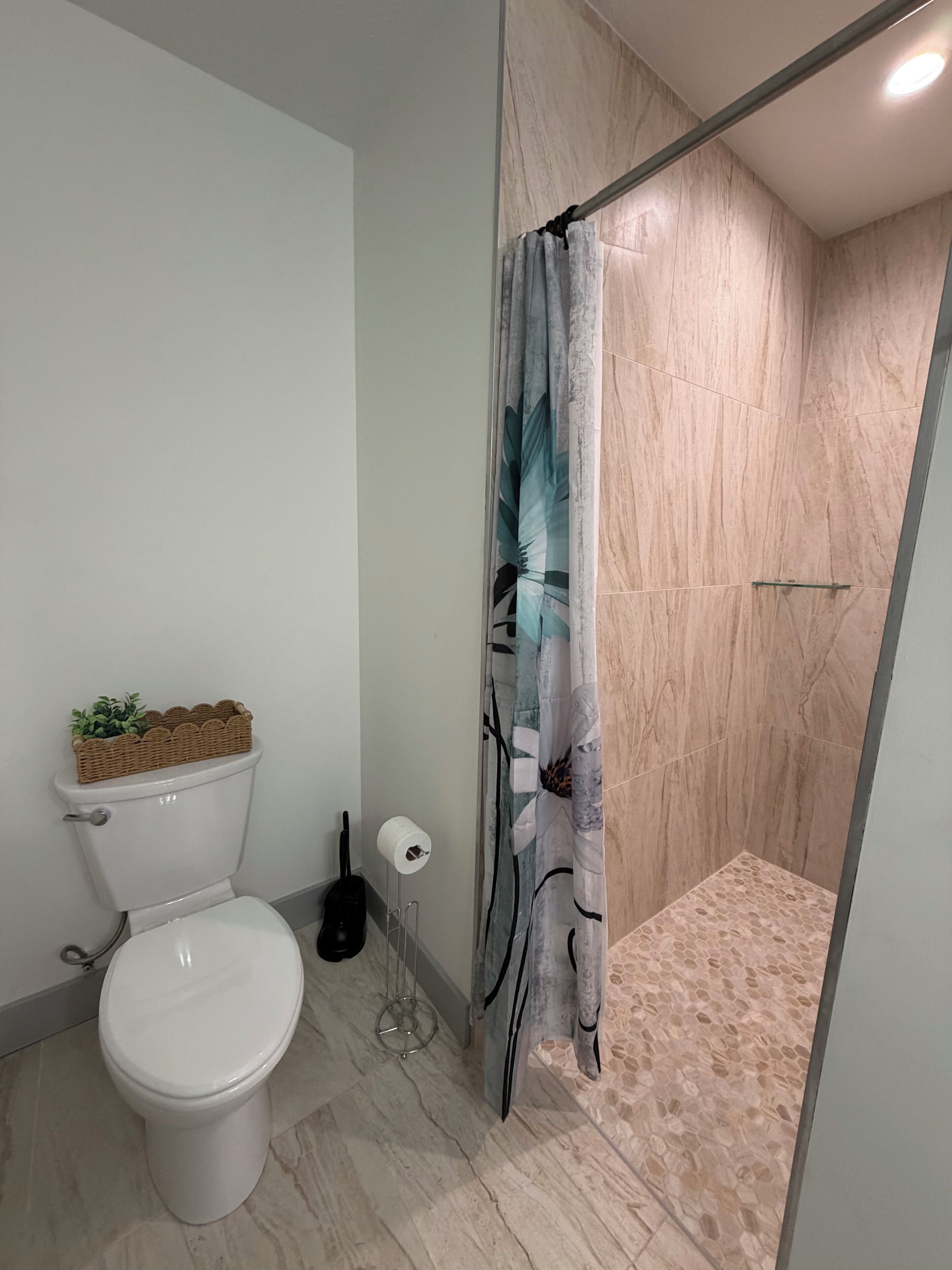 A bathroom with a toilet, a shower with a patterned floor, and a curtain with a leaf design.