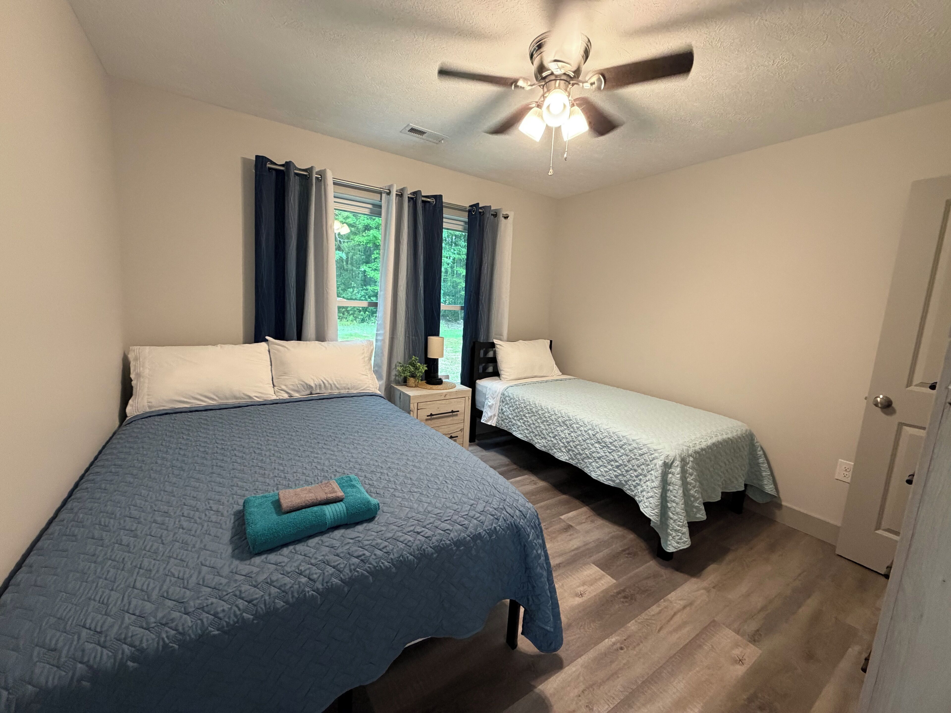 Une chambre avec deux lits, un ventilateur de plafond et une fenêtre avec des rideaux.