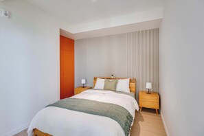 A hotel room with a bed, two bedside tables, a nightstand, a window with blinds, and a door. - 311 Cook - Apartment in Old Quebec (Québec)