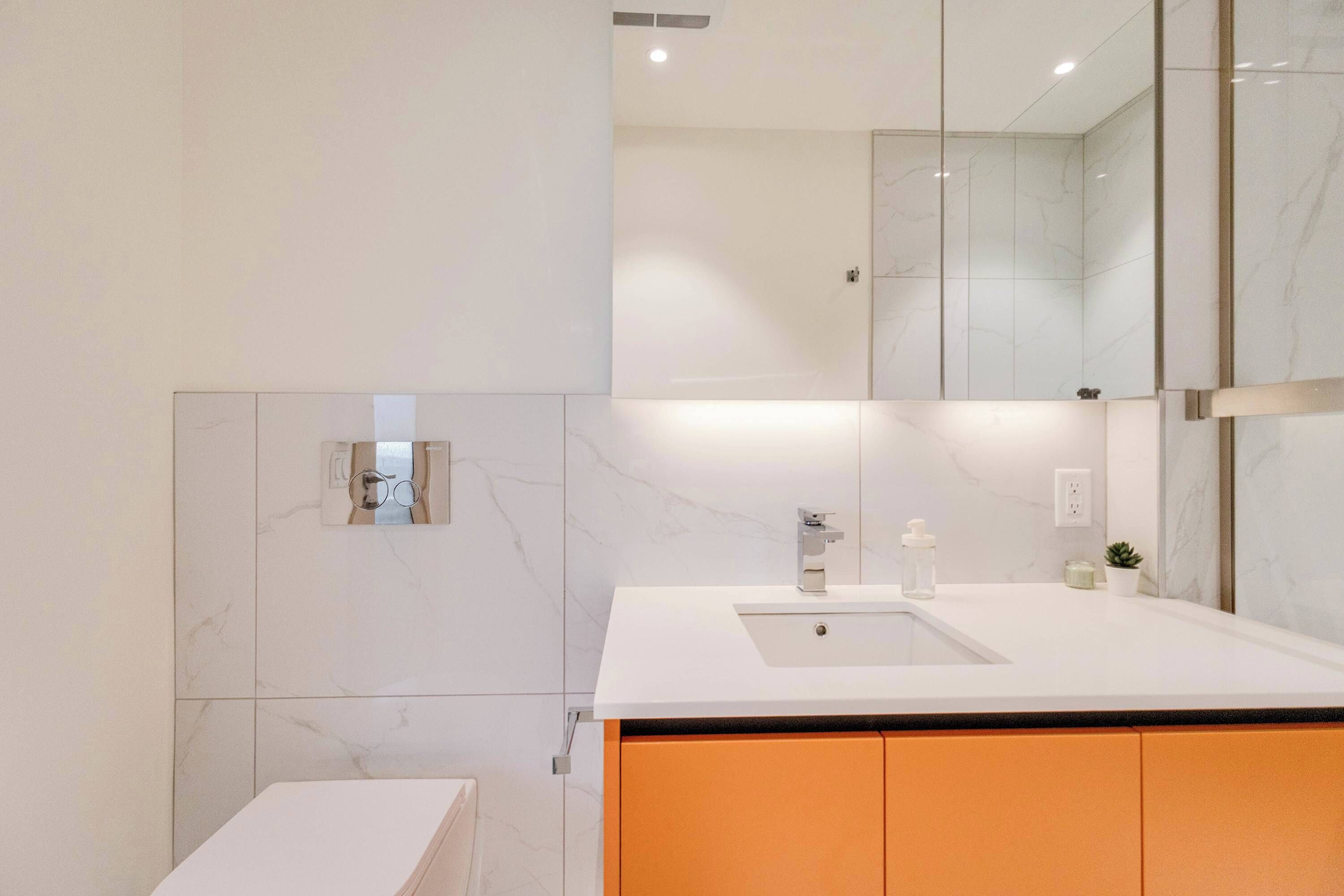 A modern bathroom with a white sink, a mirror, and a marble backsplash.