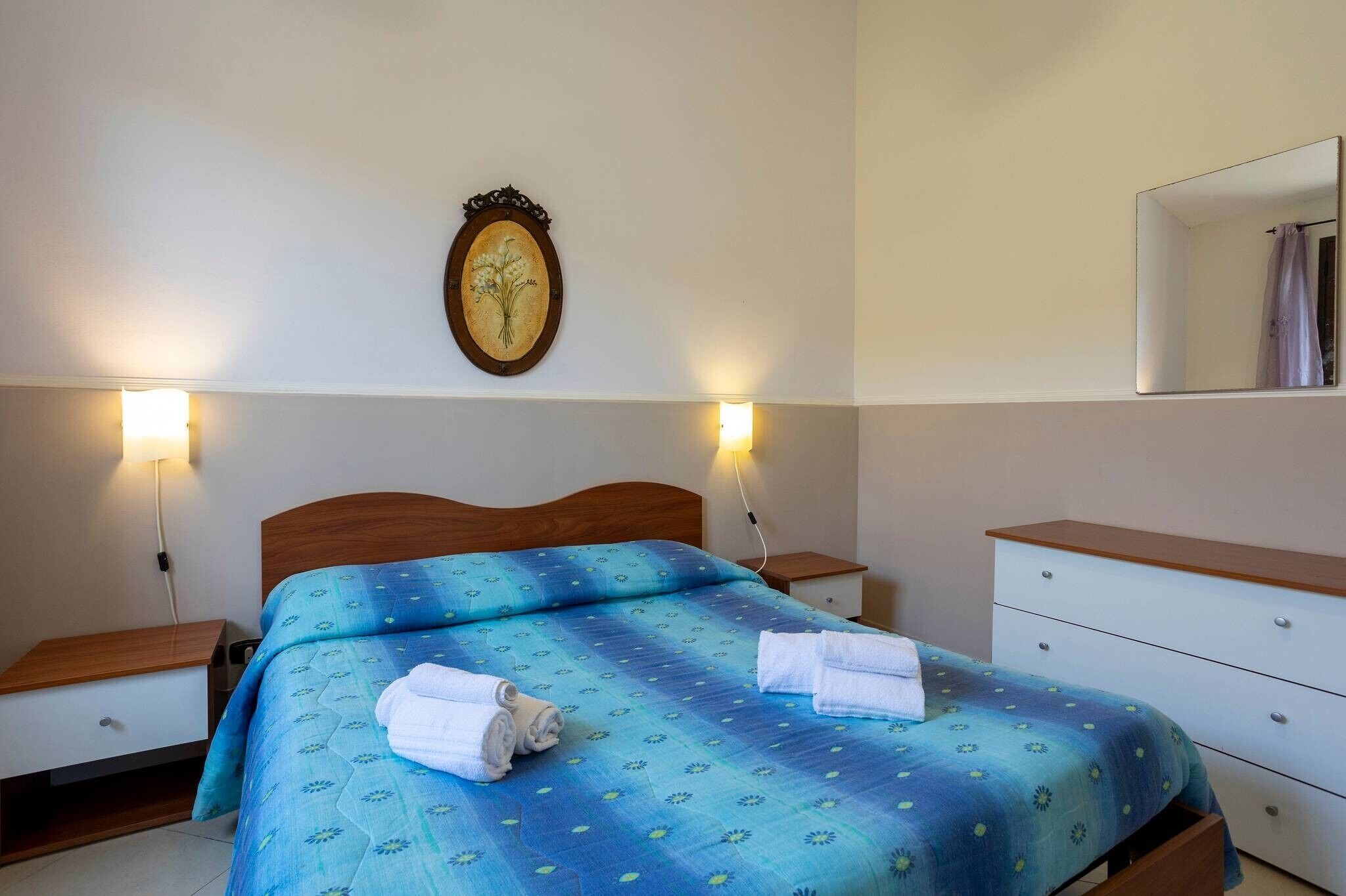 Una camera da letto con un letto, comodini, un mobiletto, uno specchio e lampade a parete.