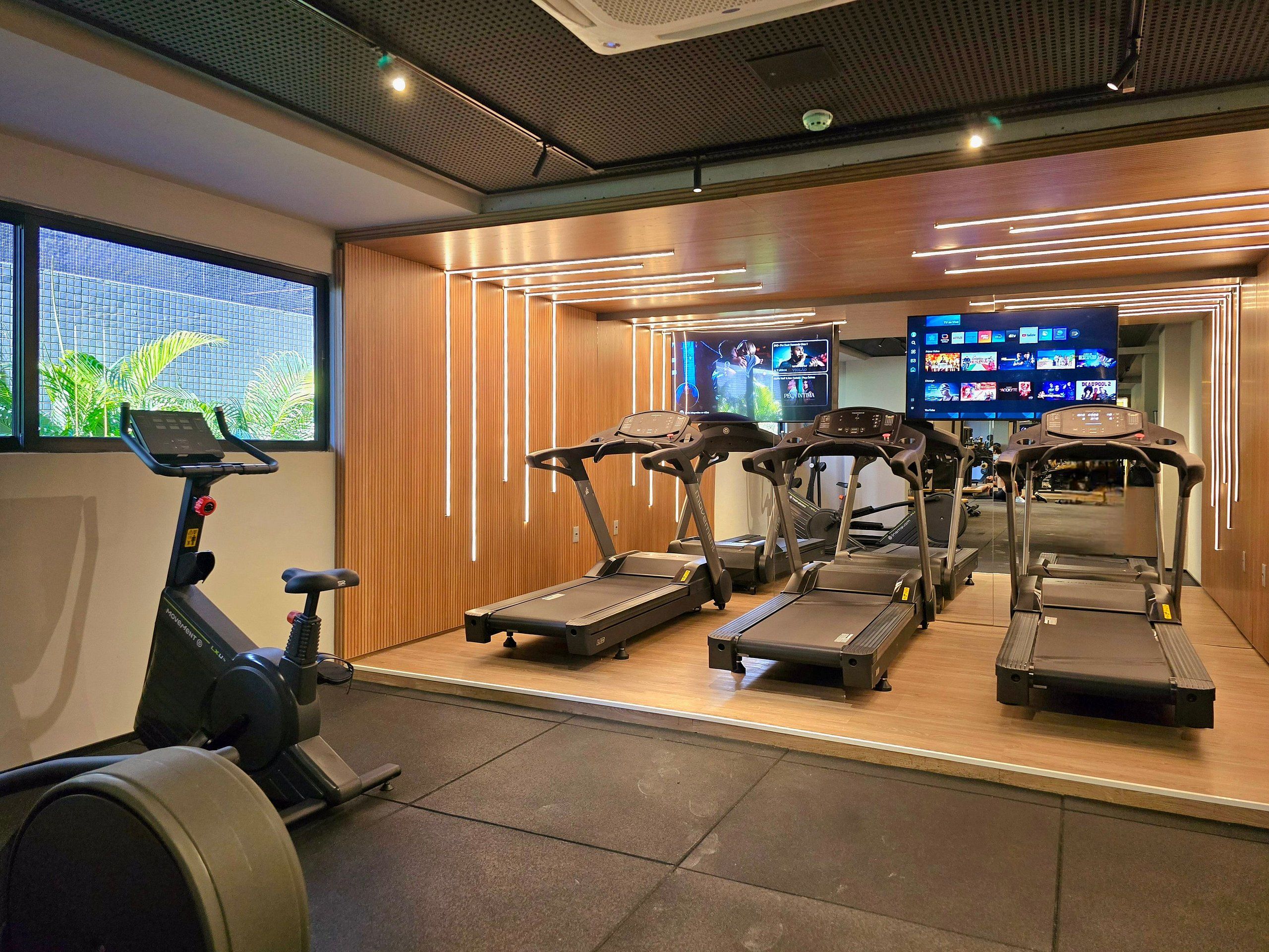 Un gimnasio con cintas de correr, una bicicleta estática y una pantalla de televisión que muestra videos de ejercicios.