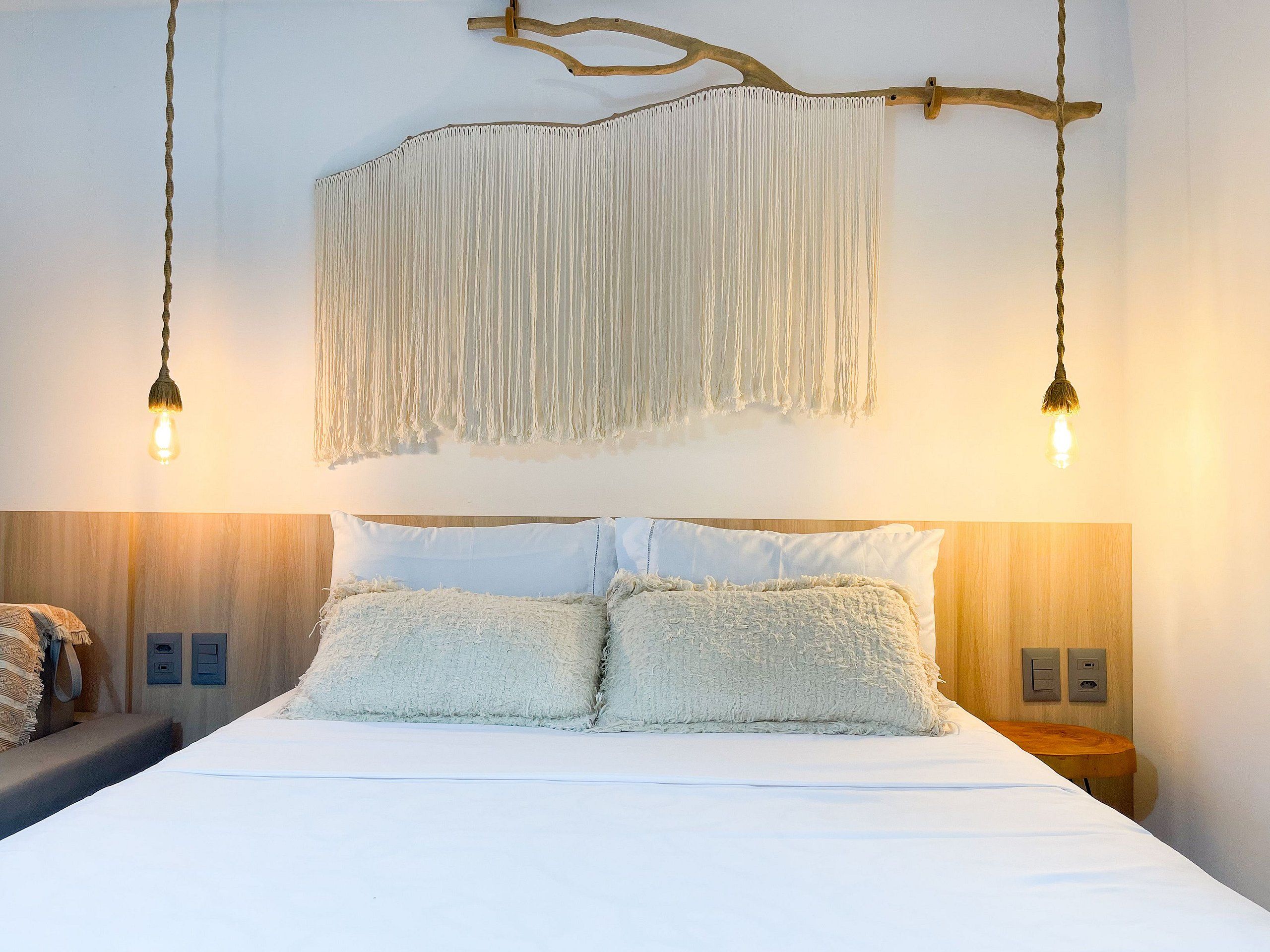 Cama com roupa de cama branca, duas almofadas e cabeceira de madeira.