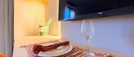 A neatly arranged dining area with a table set for two, a wine glass, and a potted plant.