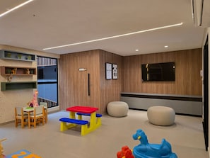 A modern children's play area with a table and chairs, a bench, and a wall-mounted TV. - Beach Haus By Hosppedar (João Pessoa)