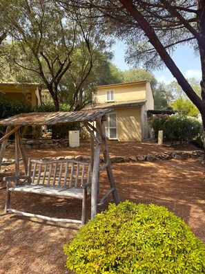 A rustic outdoor seating area with a wooden bench and a pergola structure, surrounded by a garden with a small bush and a stone wall. - Villa with a pool near Palombaggia Beach (Porto-Vecchio)