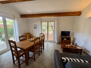 Uma sala de estar mobiliada, com uma mesa de jantar de madeira, cadeiras, um sofá, uma mesa de centro e uma televisão.