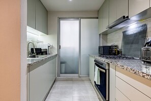 A narrow kitchen with a gas stove, microwave, and a small oven. - Group Friendly | Private Terrace & BBQ in Roma Sur (Mexico City)