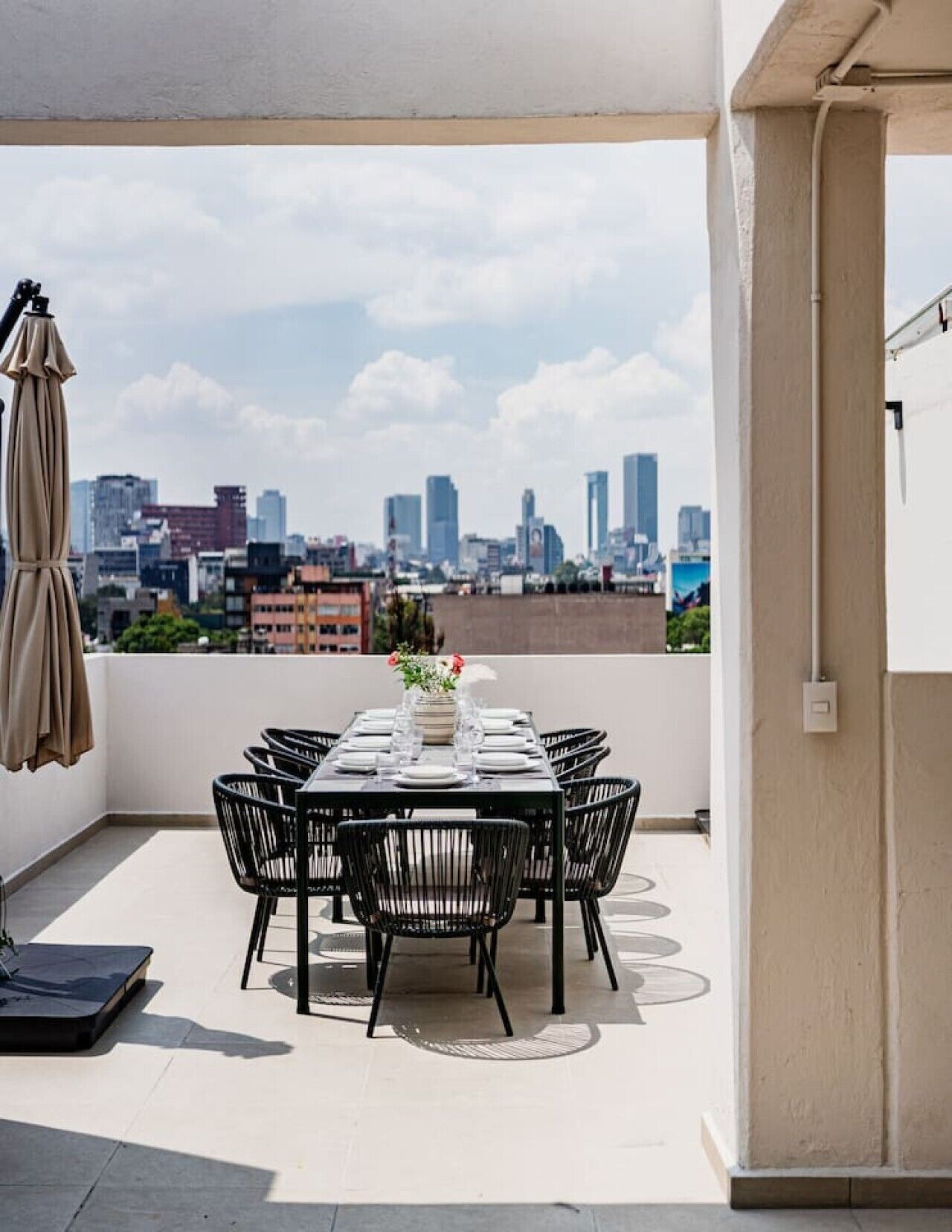 A rooftop terrace with a table set for dining, chairs, and a city skyline view.