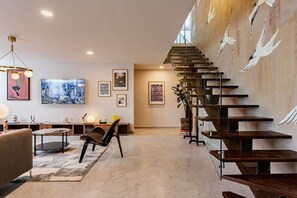 A modern interior with a staircase, a cityscape painting, and a minimalist seating area. - Group Friendly | Private Terrace & BBQ in Roma Sur (Mexico City)